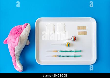 Jouet de dauphin en peluche par plateau d'injections de vaccin et de lolipop sur fond bleu Banque D'Images