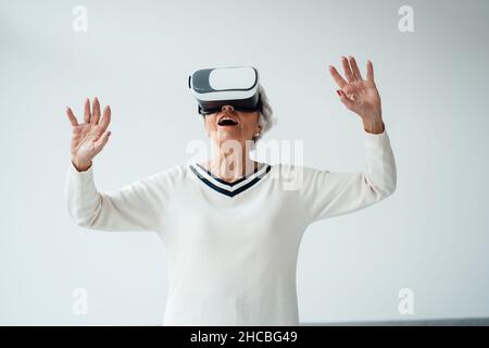 Femme âgée avec les mains levées écoutant de la musique par le biais d'un casque à la maison Banque D'Images