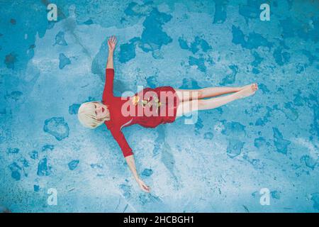 Femme flottant avec une rose jaune dans la piscine Banque D'Images