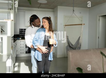 Femme enceinte vaporisant de l'eau sur les plantes de maison et parlant à travers le casque à la maison Banque D'Images