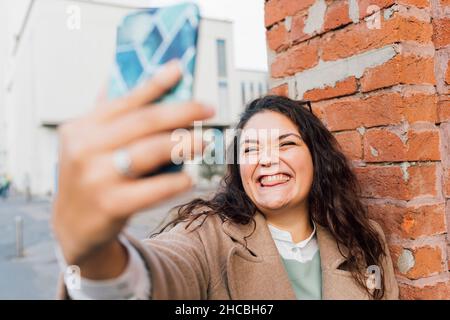 Femme aux courbes qui colle à la langue tout en prenant le selfie sur un téléphone portable Banque D'Images