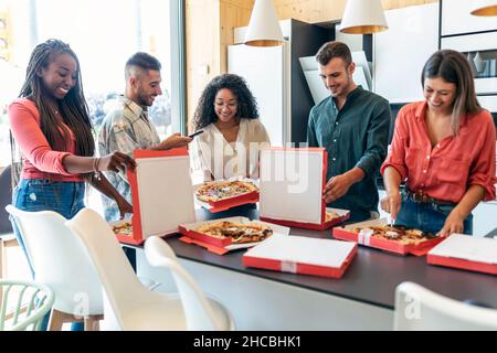 Des collègues multiraciaux heureux qui mangent de la pizza à la cafétéria du bureau Banque D'Images