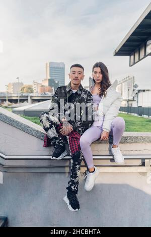 Jeune couple assis sur la main courante à des marches Banque D'Images