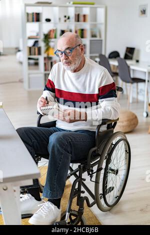 Homme d'affaires senior handicapés écrivant sur le bloc-notes dans la salle de séjour Banque D'Images
