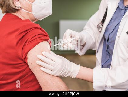 Médecin vaccinant une femme portant un masque facial à la maison Banque D'Images