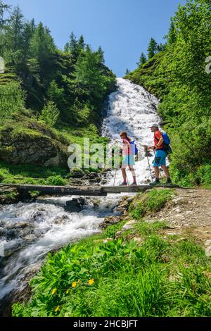 Deux randonneurs traversant le pont au-dessus de la petite cascade dans le parc national Hohe Tauern Banque D'Images