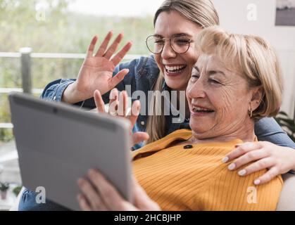 Des femmes souriantes se font passer la main pour passer des appels vidéo sur un Tablet PC à la maison Banque D'Images