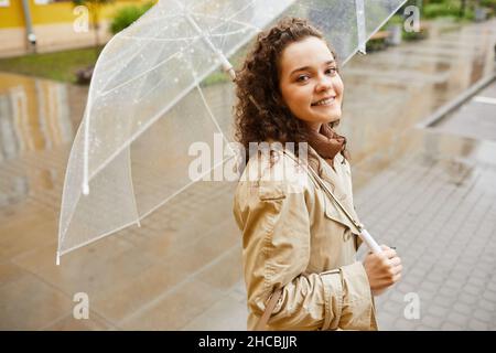 Portrait horizontal haut angle moyen de la belle jeune femme caucasienne portant un trench beige debout à l'extérieur sous un parapluie le jour des pluies smili Banque D'Images