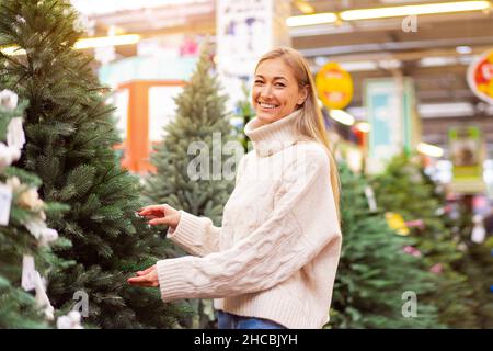 Choix de l'arbre de Noël.Belle femme d'âge moyen choisir artificiel sapin de Noël centre commercial intérieur.Caucasienne femme vêtue blanc chandail acheter arbre nouvel an heureux sourire Holiday concept Banque D'Images