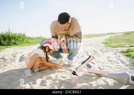 Père regardant la fille jouer avec le sable le jour ensoleillé Banque D'Images