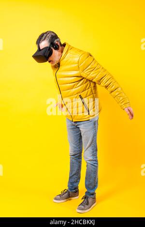 Homme souriant utilisant un casque de réalité virtuelle sur fond jaune Banque D'Images