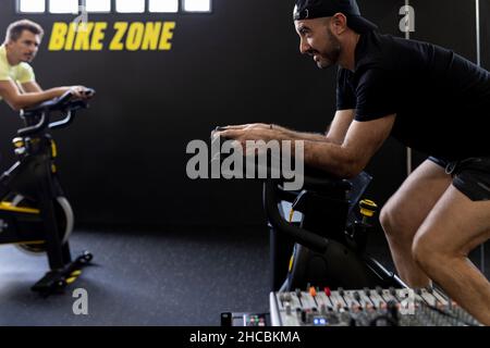 Instructeur de fitness faisant un geste sur un vélo d'exercice dans la salle de gym Banque D'Images