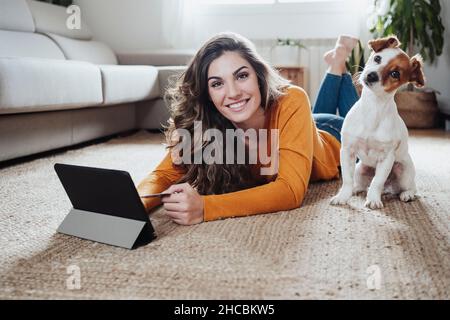 Femme avec un Tablet PC couché sur le sol avec un chien à la maison Banque D'Images