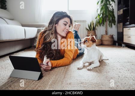 Jeune femme avec un Tablet PC regardant un chien allongé sur le sol Banque D'Images