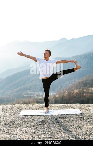 Homme s'équilibrant sur une jambe pratiquant Utthita Hasta Padangusthasana avec vue sur la montagne Banque D'Images