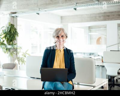 Femme d'affaires avec les mains derrière la tête se détendant sur un fauteuil sur la terrasse Banque D'Images