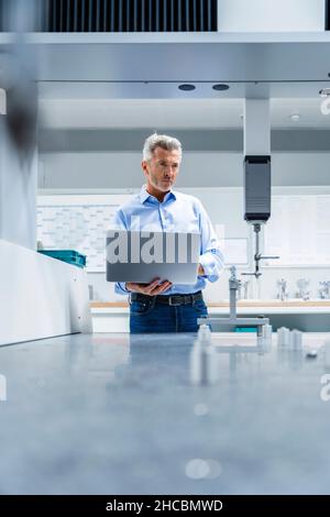 Homme d'affaires tenant un ordinateur portable à la recherche de machines automatisées dans une usine de production Banque D'Images