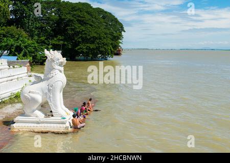 Les gens se baignent et se lavent sur la rive de la rivière Irrawaddy, à côté des statues de chinthe, en Birmanie Banque D'Images