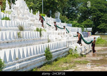 Les gens se baignent et se lavent sur la rive de la rivière Irrawaddy, à côté des statues de chinthe, en Birmanie Banque D'Images