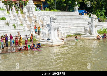 Les gens se baignent et se lavent sur la rive de la rivière Irrawaddy, à côté des statues de chinthe, en Birmanie Banque D'Images