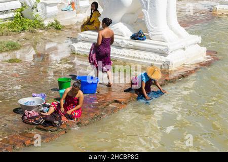 Les gens se baignent et se lavent sur la rive de la rivière Irrawaddy, à côté des statues de chinthe, en Birmanie Banque D'Images