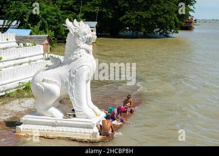 Les gens se baignent et se lavent sur la rive de la rivière Irrawaddy, à côté des statues de chinthe, en Birmanie Banque D'Images