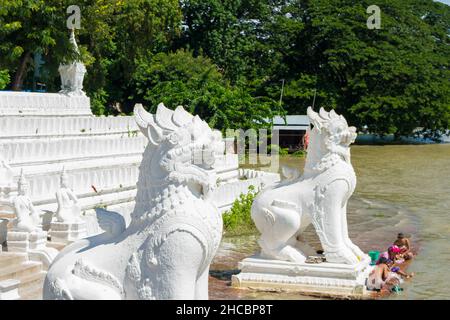 Les gens se baignent et se lavent sur la rive de la rivière Irrawaddy, à côté des statues de chinthe, en Birmanie Banque D'Images