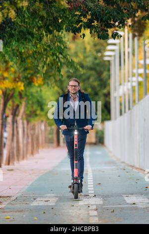 Homme d'affaires voyageant à travers le scooter électrique de poussée sur la route Banque D'Images