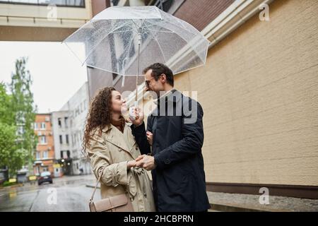 Portrait horizontal moyen d'un homme et d'une femme caucasiens qui passent du temps ensemble à l'extérieur en marchant sous un parapluie et en discutant Banque D'Images