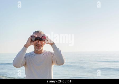 Smiling man looking through binoculars Banque D'Images