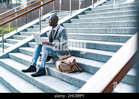 Homme d'affaires en long manteau assis avec un ordinateur portable sur les marches Banque D'Images