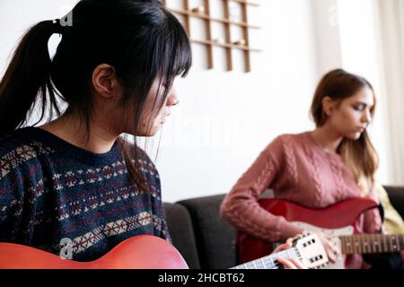 Jeunes amis jouant des guitares ensemble à la maison Banque D'Images