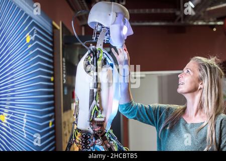 Un développeur technique souriant touche le visage du robot humain à l'atelier Banque D'Images