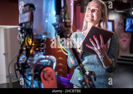 Technicien souriant avec une tablette PC qui regarde le robot humain en atelier Banque D'Images