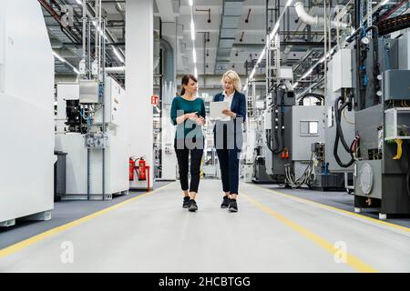 Femme d'affaires expliquant à l'usine comment un PC tablette est utilisé par un collègue Banque D'Images