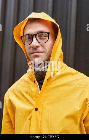 Gros plan vertical moyen d'un homme adulte portant un imperméable jaune debout à l'extérieur le jour de la pluie regardant l'appareil photo Banque D'Images