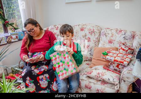 Mère et son fils se sont assis ensemble sur un cadeau d'ouverture de seettee le jour de Noël Banque D'Images