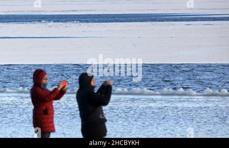 27 décembre 2021, Mecklembourg-Poméranie occidentale, Dierhagen : un homme et une femme se tiennent au port partiellement gelé de Bodden, sur la péninsule de Fischland, en mer Baltique.Le gel intense a causé la première glace sur l'eau.Photo: Bernd Wüstneck/dpa-Zentralbild/dpa Banque D'Images