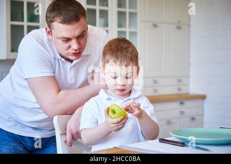 garçon avec son père dans la cuisine.L'enfant mange une pomme.Copier l'espace Banque D'Images