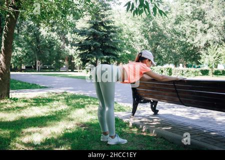 portrait d'une jeune femme sportive posant au parc dans des vêtements de sport se réchauffant s'étirant sur le banc arrière avant de courir Banque D'Images