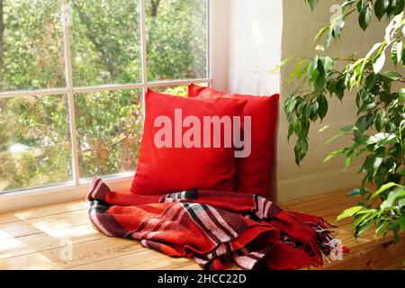 Intérieur de chambre moderne avec un seuil de fenêtre confortable, des oreillers rouges et une plante verte Banque D'Images