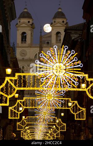 Italie, Rome, 18 décembre 2021 : la pleine lune apparaît parmi les lumières de Noël dans la rue Condotti, église de Santissima Trinita' dei Monti à backgrou Banque D'Images