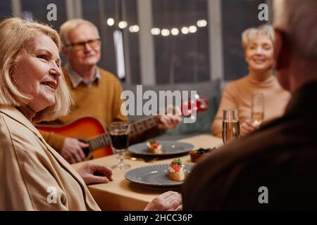 Vue sur l'épaule de la vieille femme caucasienne regardant tentement son mari assis à proximité tout en dînant avec des amis Banque D'Images