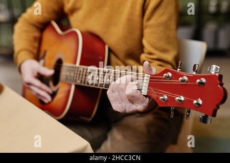 Gros plan d'un homme méconnaissable portant des vêtements décontractés assis à une table et jouant de la guitare acoustique Banque D'Images