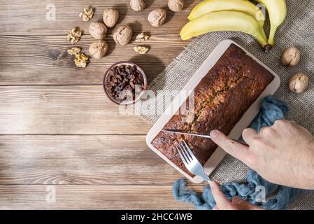 Vue en hauteur coupant un pain de banane avec des noix, des raisins secs et des bananes sur un fond de bois rustique Banque D'Images