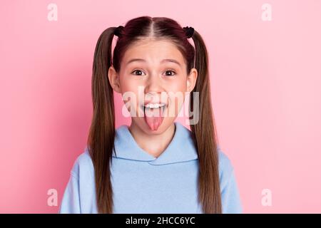 Photo portrait de l'écolière funky montrant la langue dupe ludique isolée sur fond rose pastel Banque D'Images