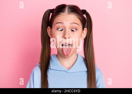 Photo portrait de l'écolière drôle montrant la langue à se moquer grimacing isolé sur fond rose pastel Banque D'Images