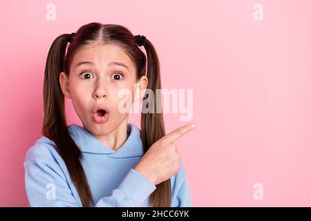 Photo portrait d'une écolière surprise montrant le doigt de promotion d'espace de copie isolé sur fond rose pastel Banque D'Images