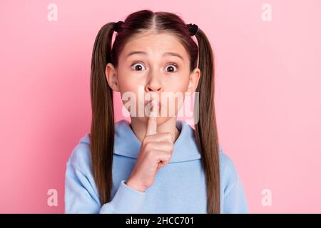 Photo portrait de petite écolière mettre le doigt près des lèvres en regardant en gardant secret isolé sur fond rose pastel Banque D'Images