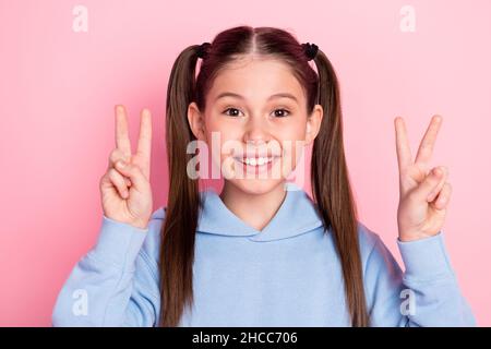 Photo portrait d'une écolière montrant un geste de signe en V souriant isolé sur fond rose pastel Banque D'Images